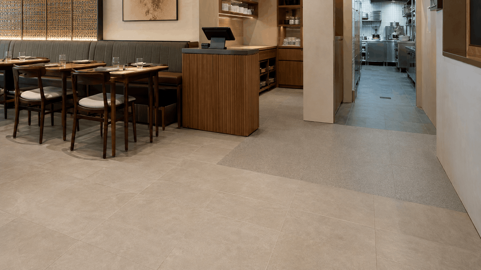 Restaurant dining area with beige tile flooring transitioning into darker anti-slip tile at the commercial kitchen entrance